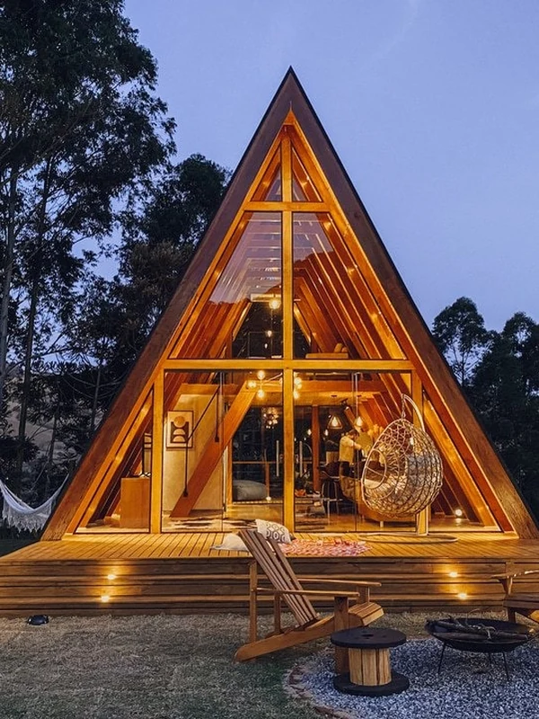A Cabana do Sossego, A-frame de madeira iluminada à noite, com a fogueira acesa