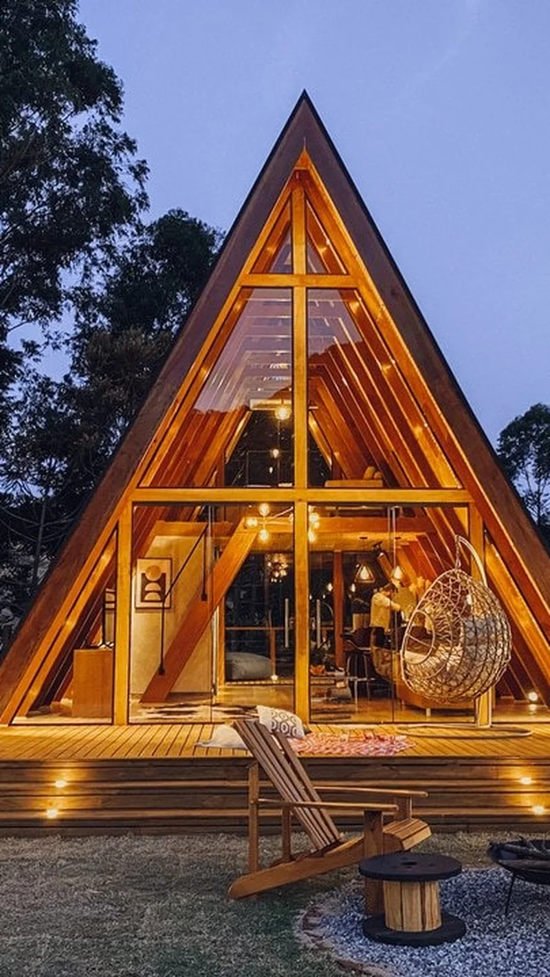 Cabana A-frame iluminada ao entardecer, com a fogueira acesa no gramado